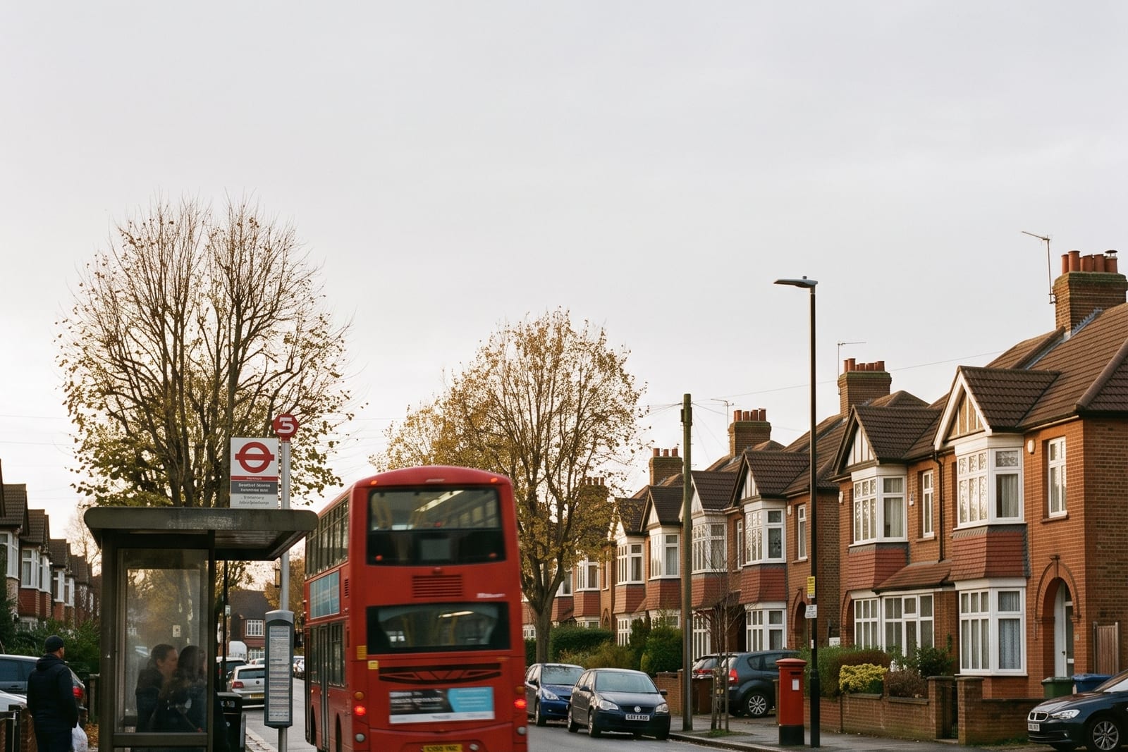 A red bus on a residential London street in autumn.
